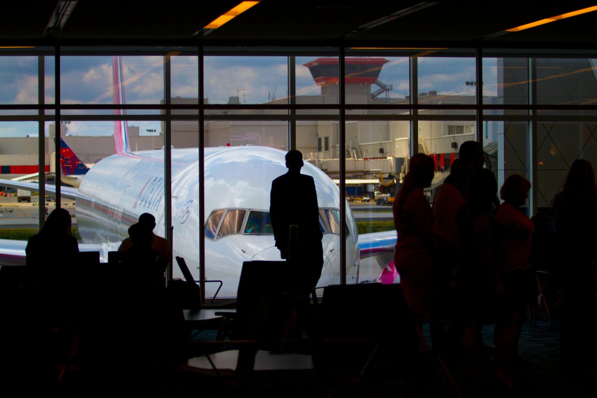 Silhouettes of travelers waiting at an airport terminal with an airplane visible through the window.